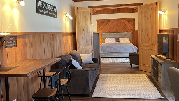 A cozy room with a wooden ceiling, a bed with a herringbone headboard, a sofa, a coffee table, and a bar area with stools. - One Bedroom Cottage (Half Moon Bay)
