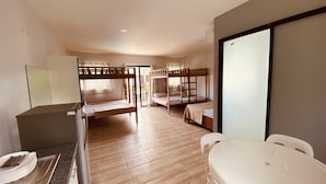 A hotel room with a wooden bunk bed, a desk with a chair, a dining table with chairs, and a large window.
