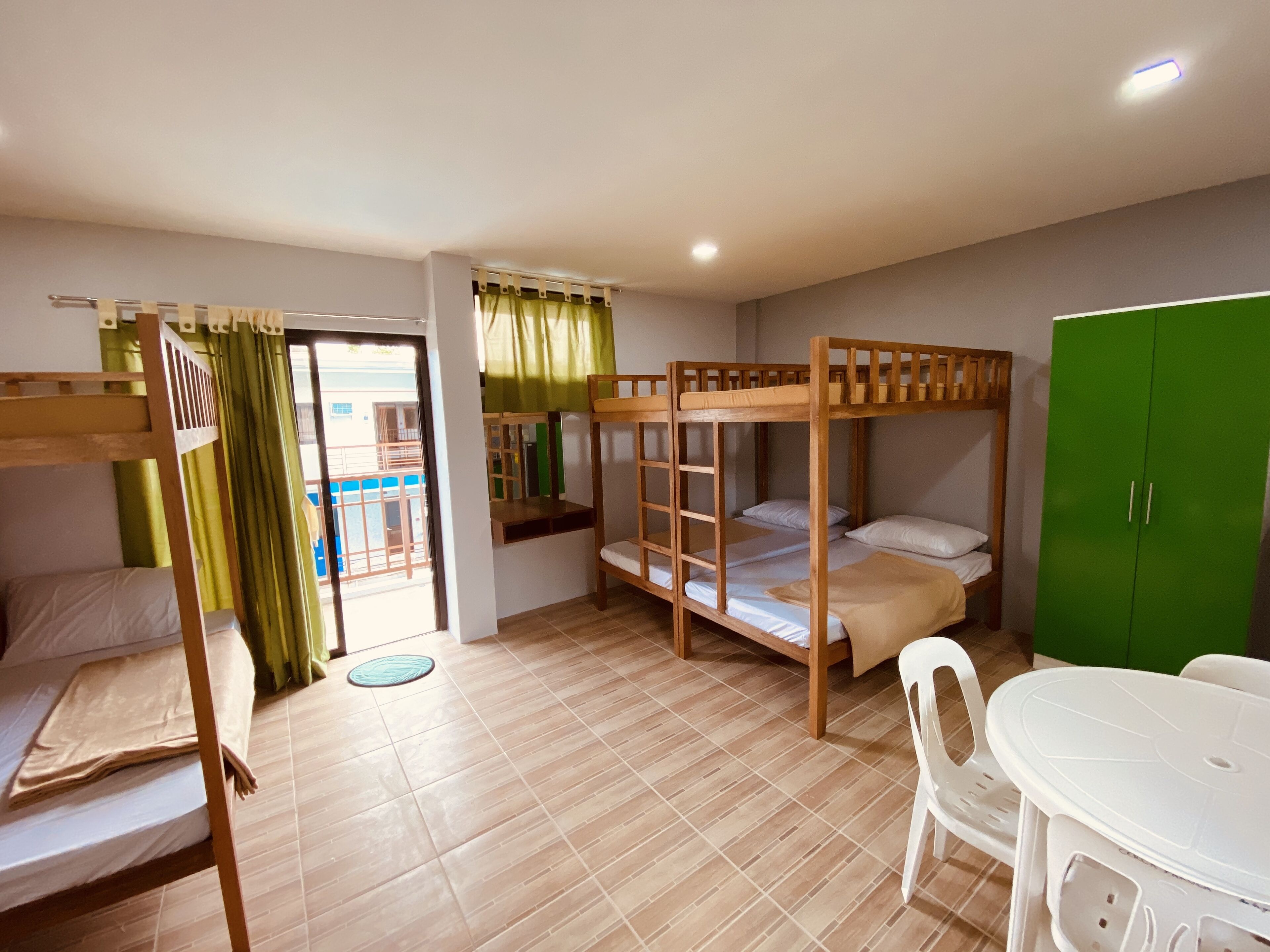 Un dormitorio con literas, un armario verde, una mesa blanca y vistas a un balcón.