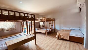 A dormitory room with bunk beds, a wooden floor, and an air conditioning unit on the wall.