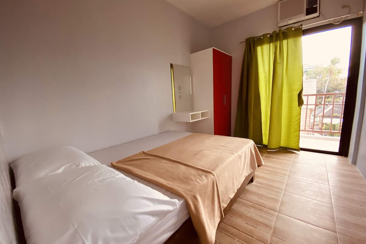 A room with a bed, a wardrobe, a mirror, and a window with curtains.