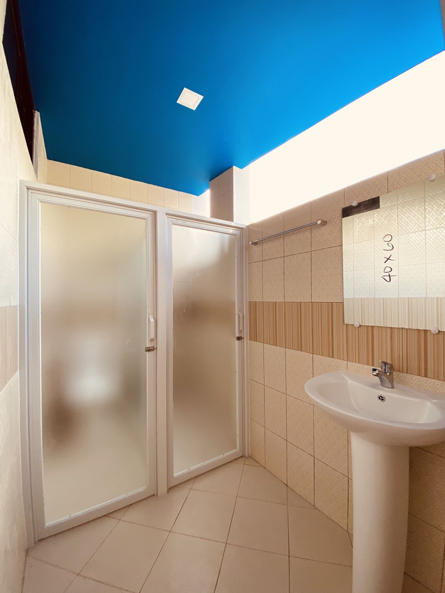 Un baño con lavamanos blanco, un espejo y una puerta de vidrio satinado.