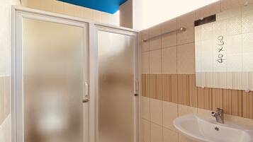Un baño con lavamanos blanco, un espejo y una puerta de vidrio satinado.