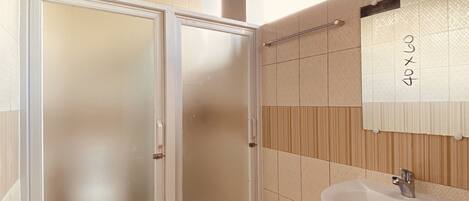 Un baño con lavamanos blanco, un espejo y una puerta de vidrio satinado.