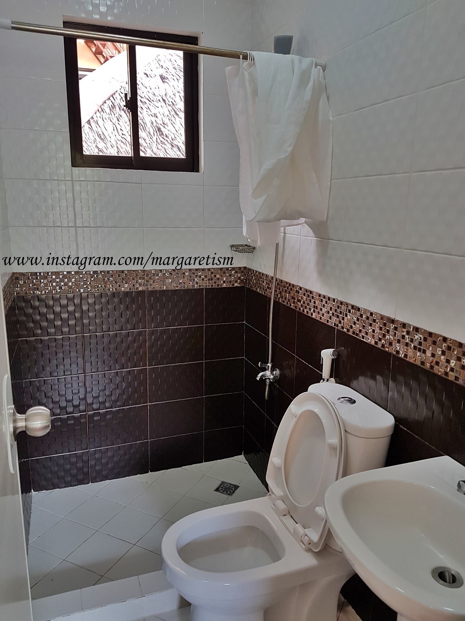 A bathroom with a toilet, sink, and shower. There is a window above the toilet.