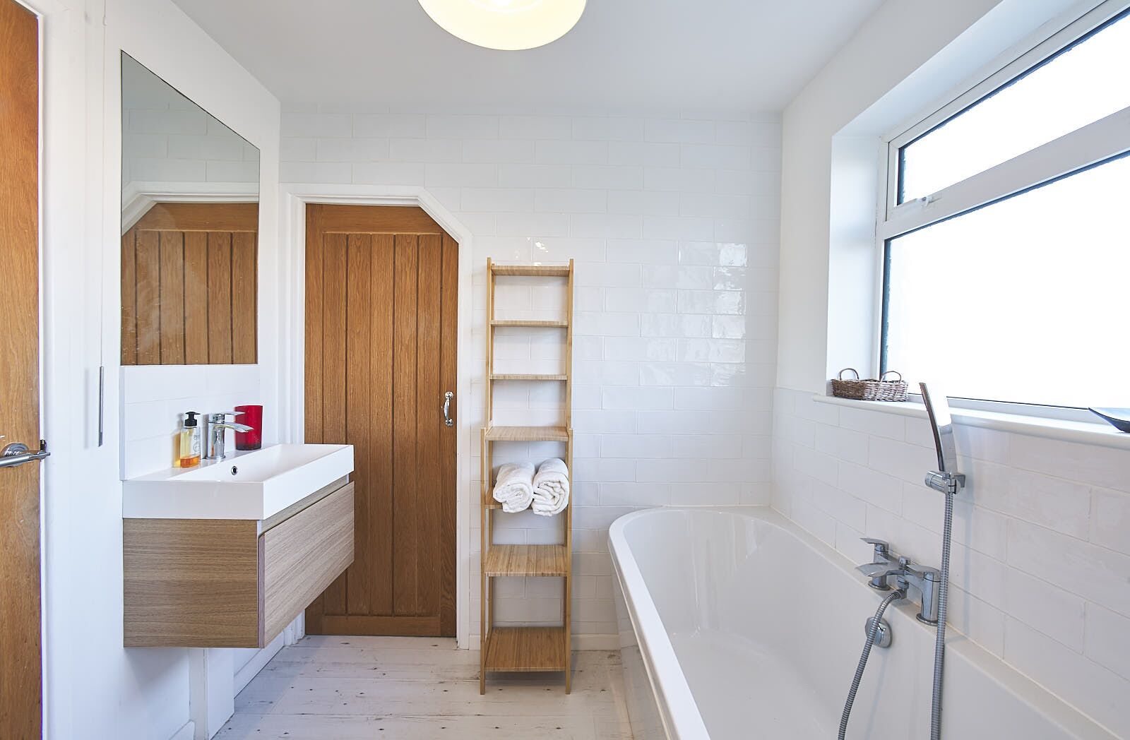 Ein modernes Badezimmer mit einem weißen Waschtisch, einer Holztür und einer freistehenden Badewanne.