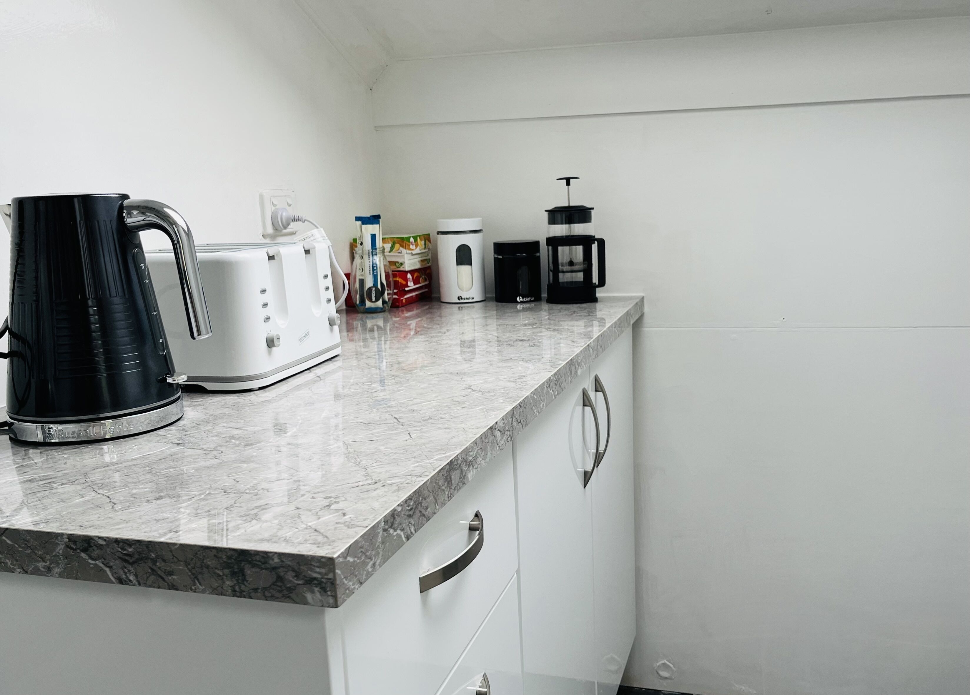 A kitchen with a marble countertop, a black coffee maker, a white toaster, and a white kettle.