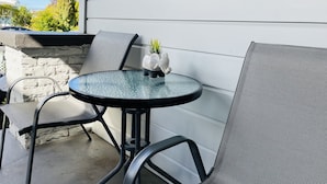 Une terrasse avec une table ronde en verre, deux chaises et une petite plante en pot.