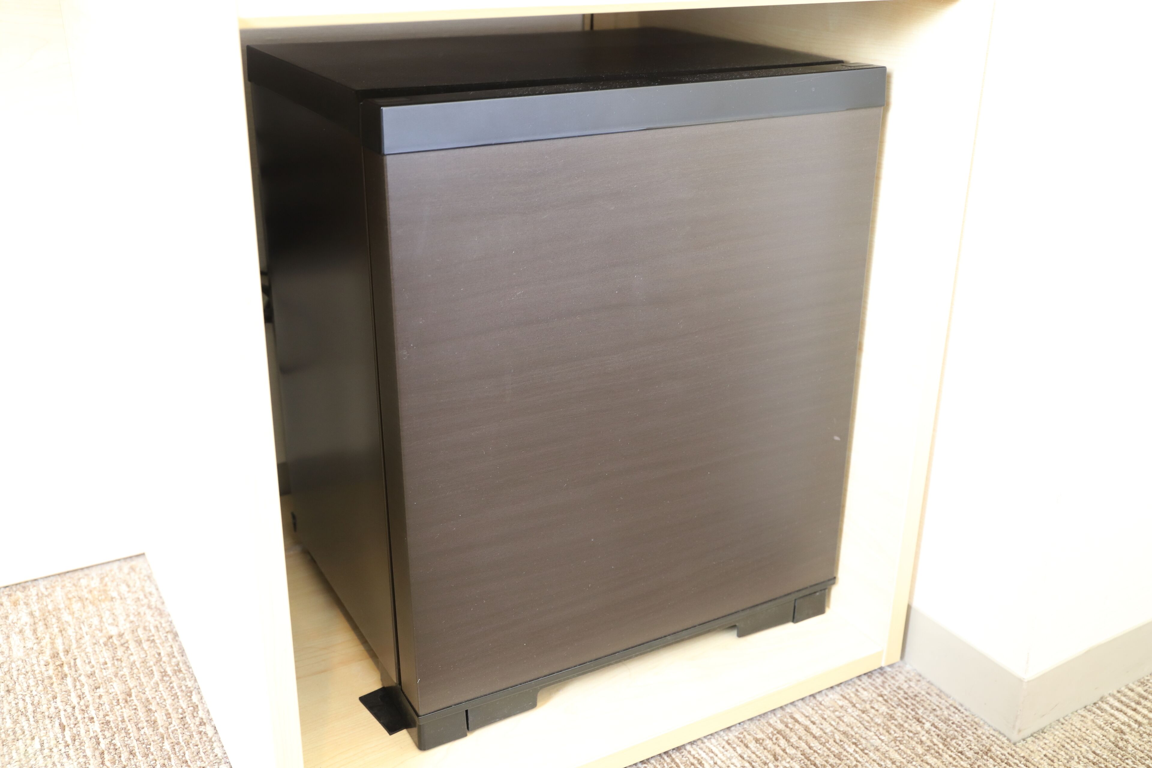 A compact, dark-colored refrigerator in a kitchen with a light-colored countertop and a textured floor.