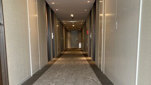 A long, narrow hallway with carpeted floors and walls lined with doors, likely leading to hotel rooms.