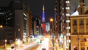 A nighttime cityscape with illuminated buildings and a prominent tower in the background.