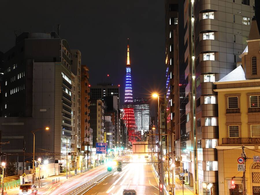 Un paisaje urbano nocturno con edificios iluminados y una torre destacada al fondo.