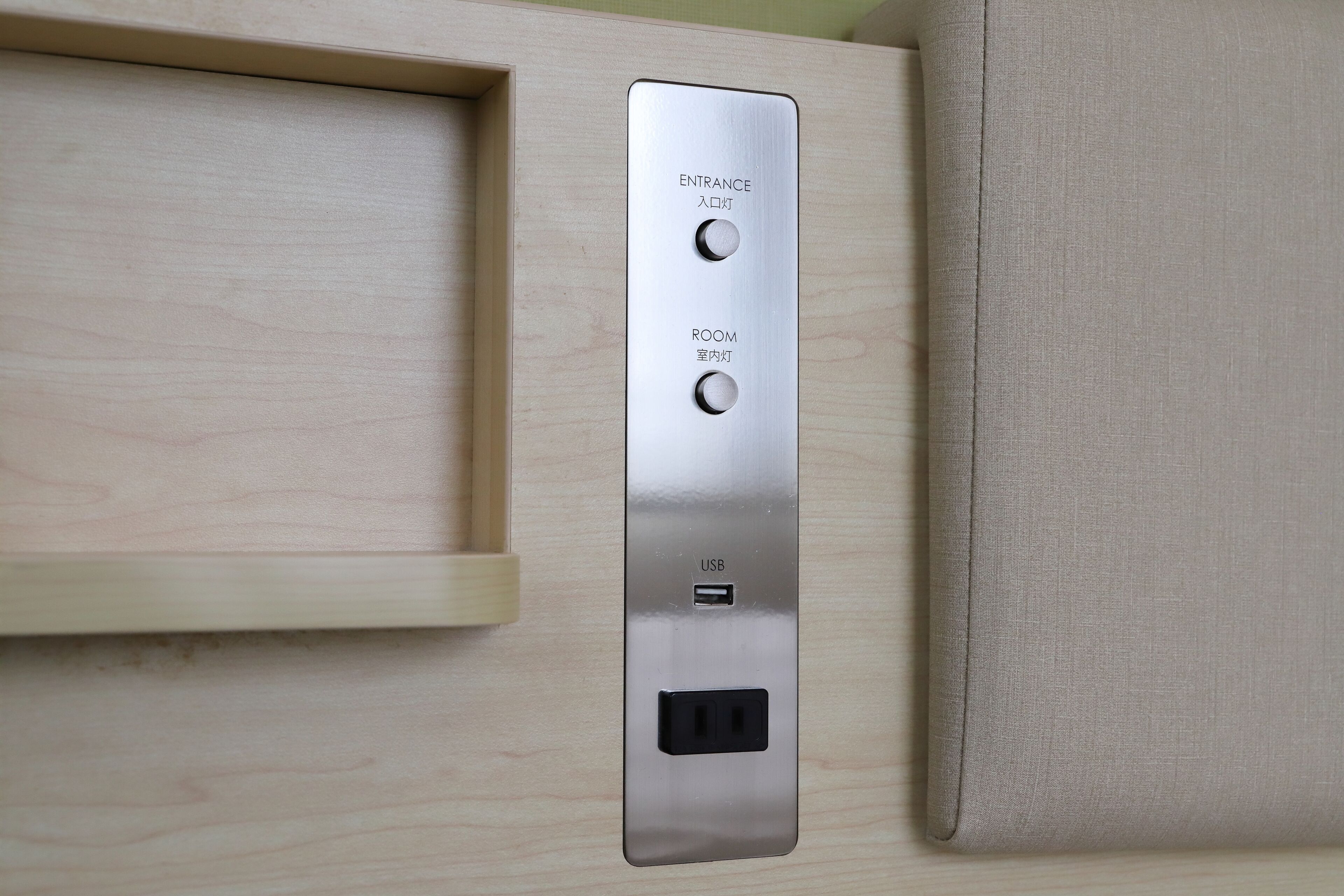 Panel de control instalado en la pared con dos botones etiquetados 'Entrada' y 'Habitación' y un puerto USB.