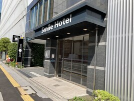 Moderni hotellin sisäänkäynti, jossa on suuri lasijulkisivu, kyltti, jossa lukee ”Smile Hotel”, ja pieni puutarha-alue, jossa on kasveja.
