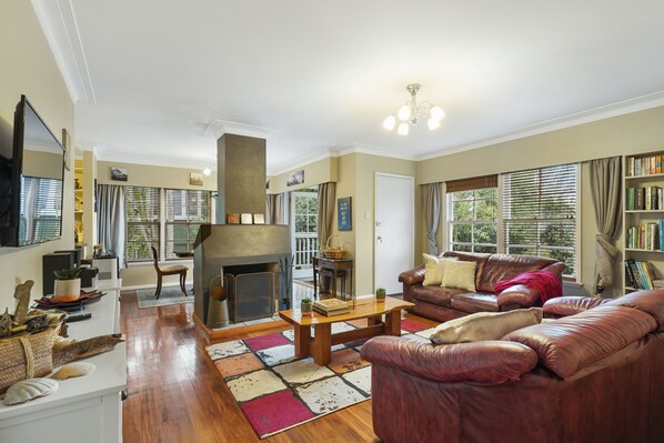 A spacious living room with a fireplace, leather sofas, a coffee table, and a bookshelf. - Kohi Family Home- Netflix & Gardens View (Auckland)
