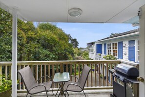 A covered outdoor area with a grill, two chairs, and a table. - Kohi Family Home- Netflix & Gardens View (Auckland)