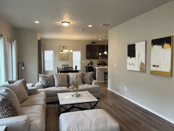 Relax in this stylish living room with a sectional sofa, coffee table, and ottoman, surrounded by abstract art and a dining area.