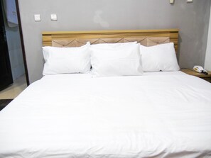 A neatly made bed with white linens and a wooden headboard.