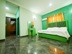 A bedroom with a green bed, a small bedside table, a mirror, and a green wall.