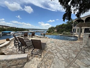 Un patio de piedra con mobiliario exterior, una piscina y vistas a un puerto deportivo.