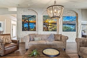 A living room with a sofa, armchairs, and a coffee table. There are three paintings on the wall. - Lake Views + Pool & Waterfall - Lake Travis Vista! (Austin)