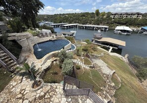 A swimming pool with a stone deck, a grassy area, and a view of boats on the water.