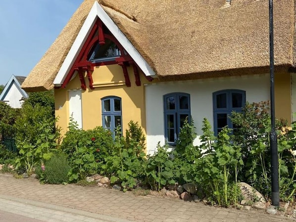 A house with a thatched roof, yellow exterior walls, and blue window frames.