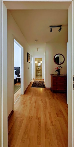 Un pasillo con piso de madera que lleva a un dormitorio con cama y mesita de noche.