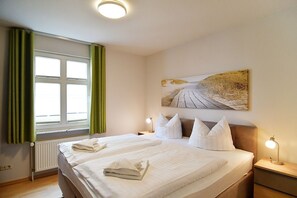 A hotel room with two beds, a large window with green curtains, a painting on the wall, and bedside lamps. - Haus Miramar Appartement 15 - Haus Miramar (Heringsdorf)