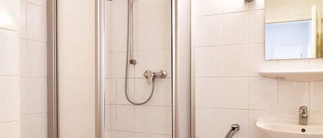 A bathroom with a glass-enclosed shower, a toilet, a sink, and a trash bin.