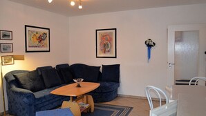 Ein Wohnzimmer mit einem blauen Sofa, einem Holztisch und gerahmten Kunstwerken an den Wänden.