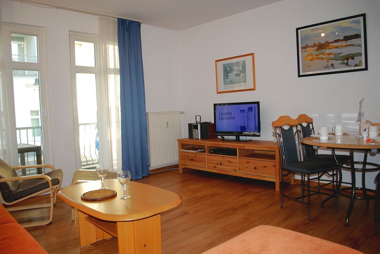A living room with a wooden table, two chairs, a sofa, a television, and a framed picture on the wall.