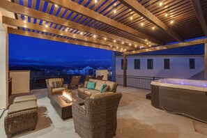 A covered outdoor patio with wicker furniture, a fire pit, and a hot tub.
