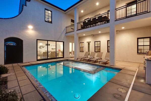 A two-story building with a swimming pool, outdoor seating, and a balcony with furniture.