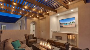 Un espace extérieur accueillant avec un foyer, des meubles en osier et un grand écran de télévision.