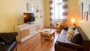 A living room with a TV, sofa, coffee table, and a window with curtains.