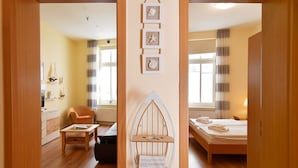 A cozy room with a wooden floor, a bed with a white mattress, a chair, a small table, and a wall-mounted shelf with decorative items.