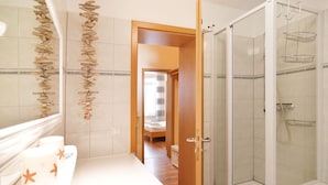 A modern bathroom with a glass shower, a wooden door leading to a bedroom, and a decorative wall with natural elements.
