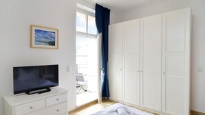 Una camera da letto con una TV sopra un comò, un armadio grande e una finestra con tende.
