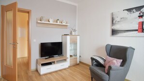 Un soggiorno con televisore su un supporto in legno, una poltrona grigia e una mensola con oggetti decorativi.