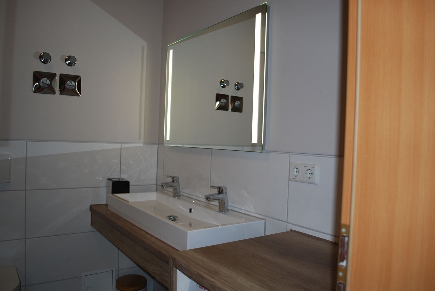 Une salle de bain moderne avec un lavabo blanc, un miroir et un plan de travail en bois.