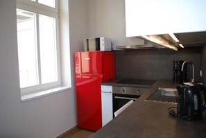 Een kleine keuken met een rode koelkast, een inbouwoven, een koffiezetapparaat en een spoelbak.