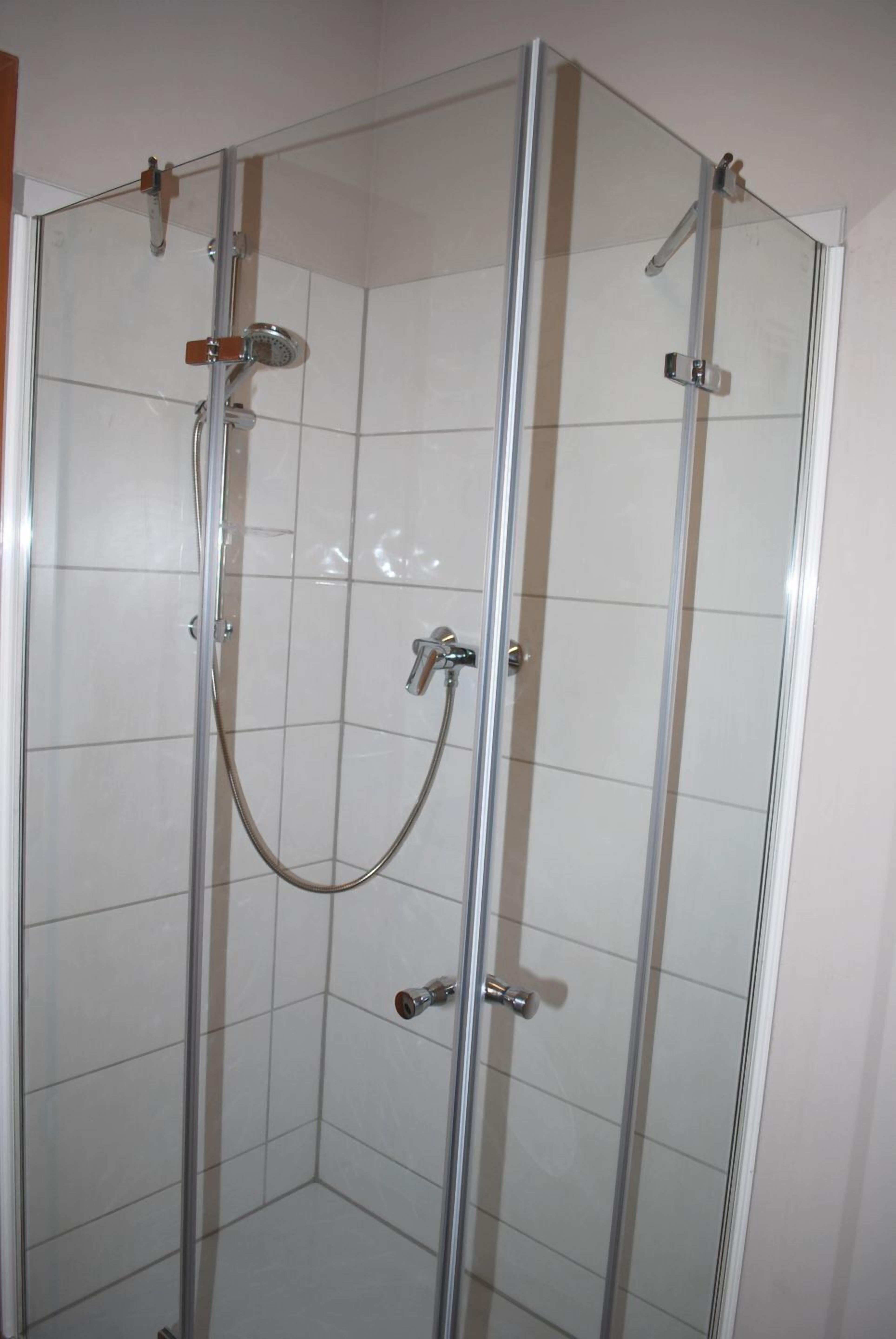 Et brusebad med glasvægge, en håndbruser og en loftmonteret brusearmatur.