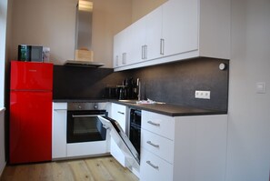 Una cucina compatta con mobili bianchi, un frigorifero rosso, un forno integrato e una lavastoviglie.