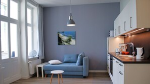 A modern kitchen with a blue sofa, a small table, and a hanging light fixture. - Haus Wanda Appartement 4a - Haus Wanda (Heringsdorf)