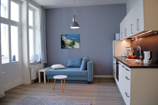 Une cuisine moderne avec un canapé bleu, une petite table et un luminaire suspendu.