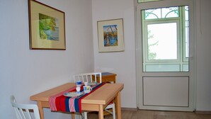 A dining area with a wooden table, white chairs, and a red and blue striped tablecloth. There are two framed pictures on the wall, and a window with a view of trees. - House Wanda Apartment 05 - House Wanda (Heringsdorf)