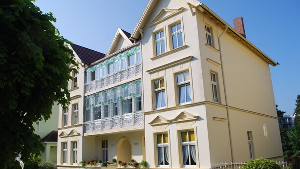 A multi-story building with a symmetrical facade, large windows, and a balcony with a metal railing. - House Wanda Apartment 05 - House Wanda (Heringsdorf)