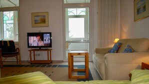 A living room with a television, a sofa, a small table, and a window with blinds. - House Wanda Apartment 05 - House Wanda (Heringsdorf)