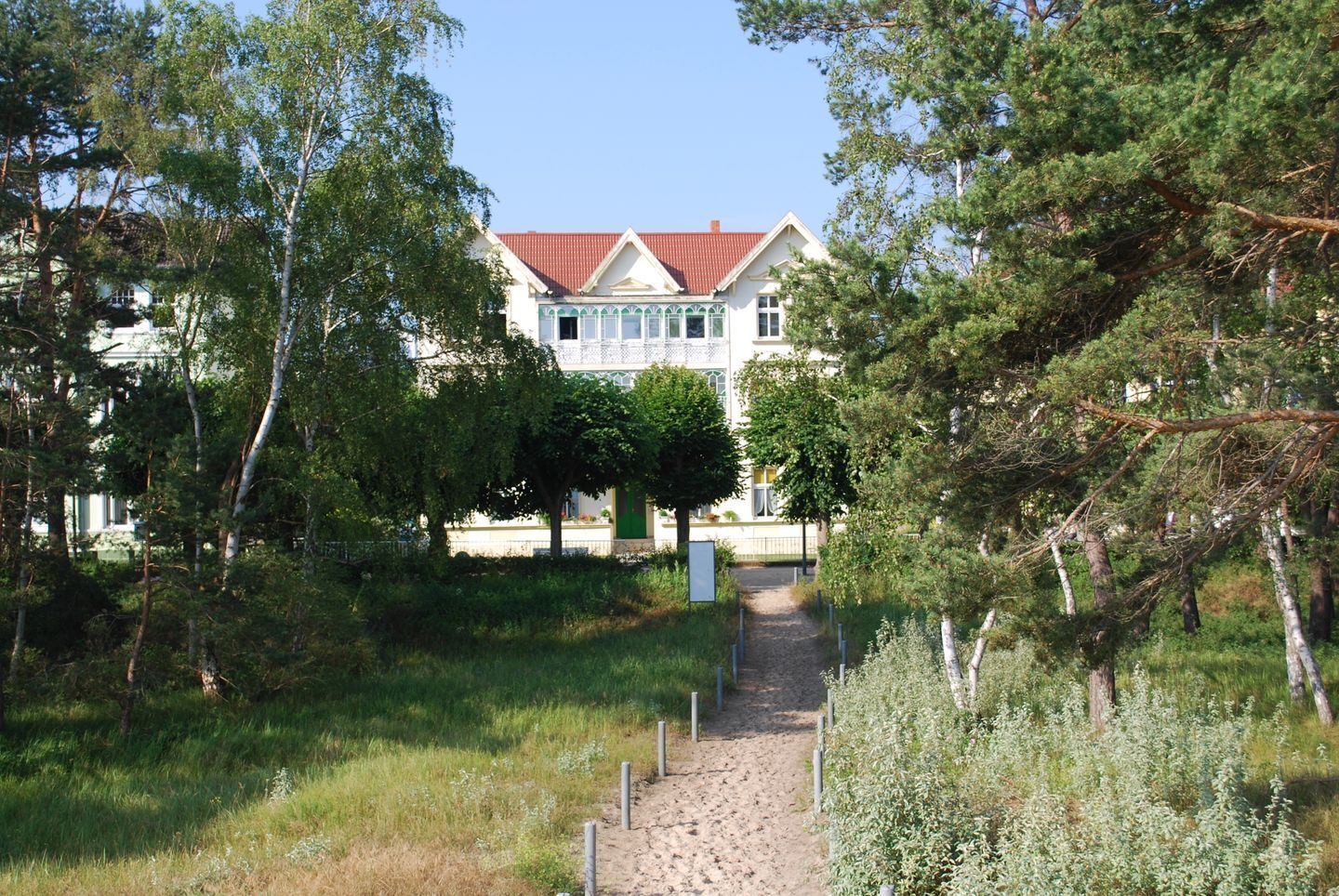 A building with a red roof and white walls, surrounded by trees and a gravel path leading to it.